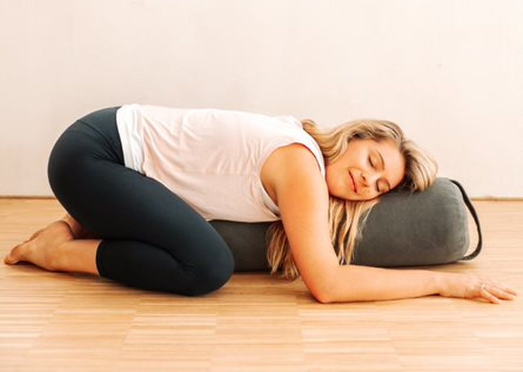 Alexandria resting over a bolster in a gentle somatic practice